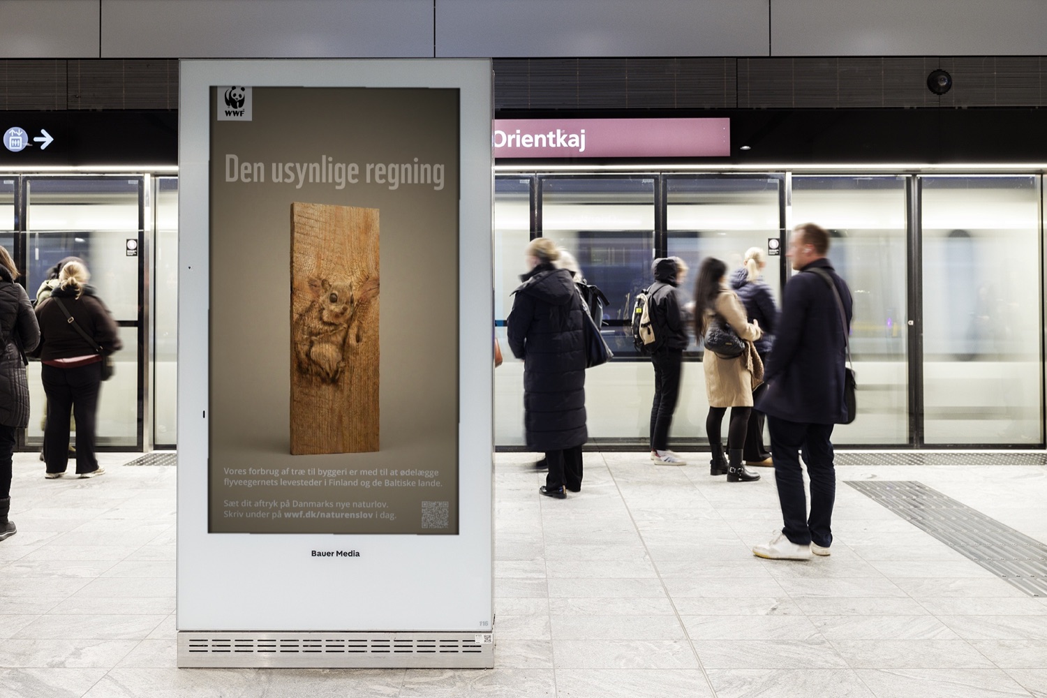Den Usynlige Regning som digital outdoor på en metrostation i København, hvor pendlere venter på toget
